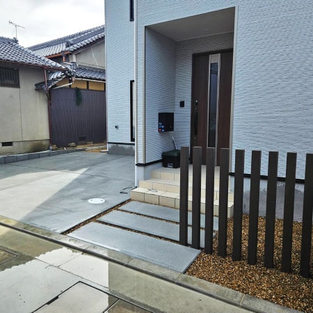 モダンな住宅の玄関アプローチ。目隠し用の縦格子フェンスと土間コンクリートの駐車場